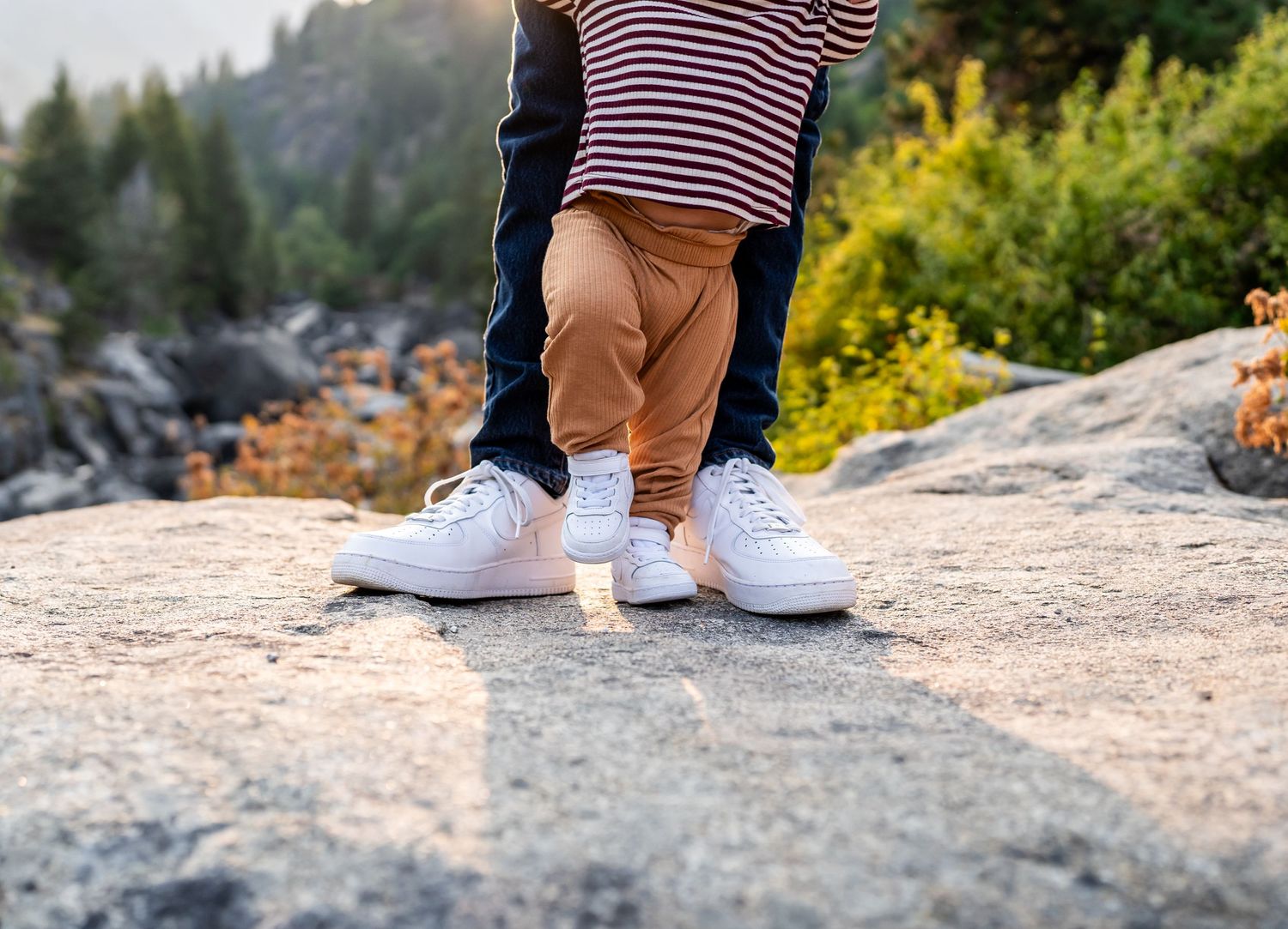 Close-up of white sneakers on a rocky mountain surface during golden hour.