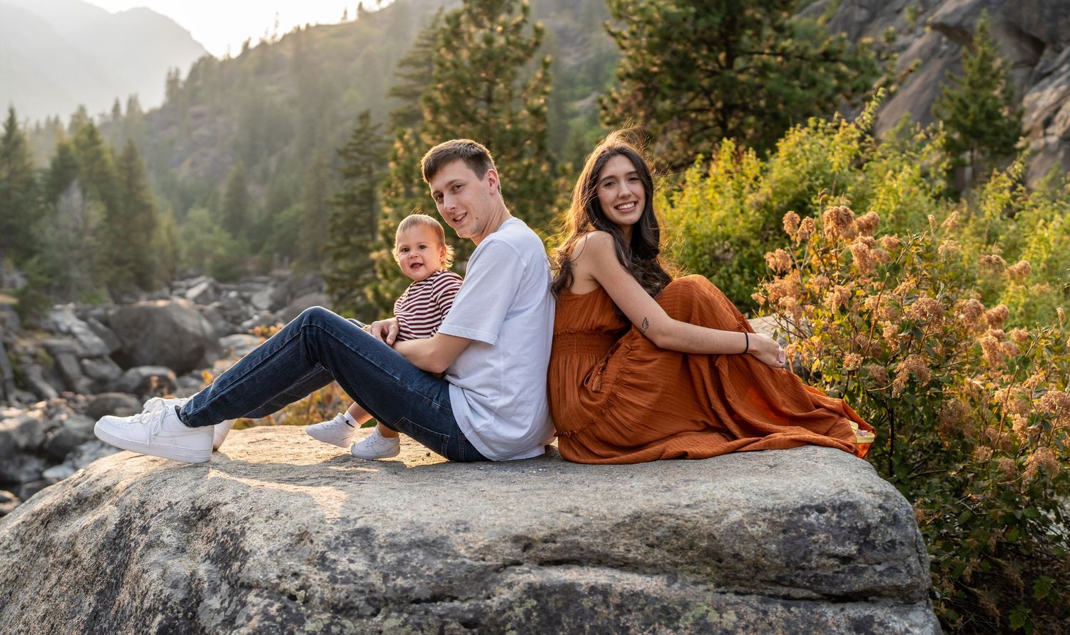 Family sharing a joyful moment on a rocky mountain ledge during sunset.