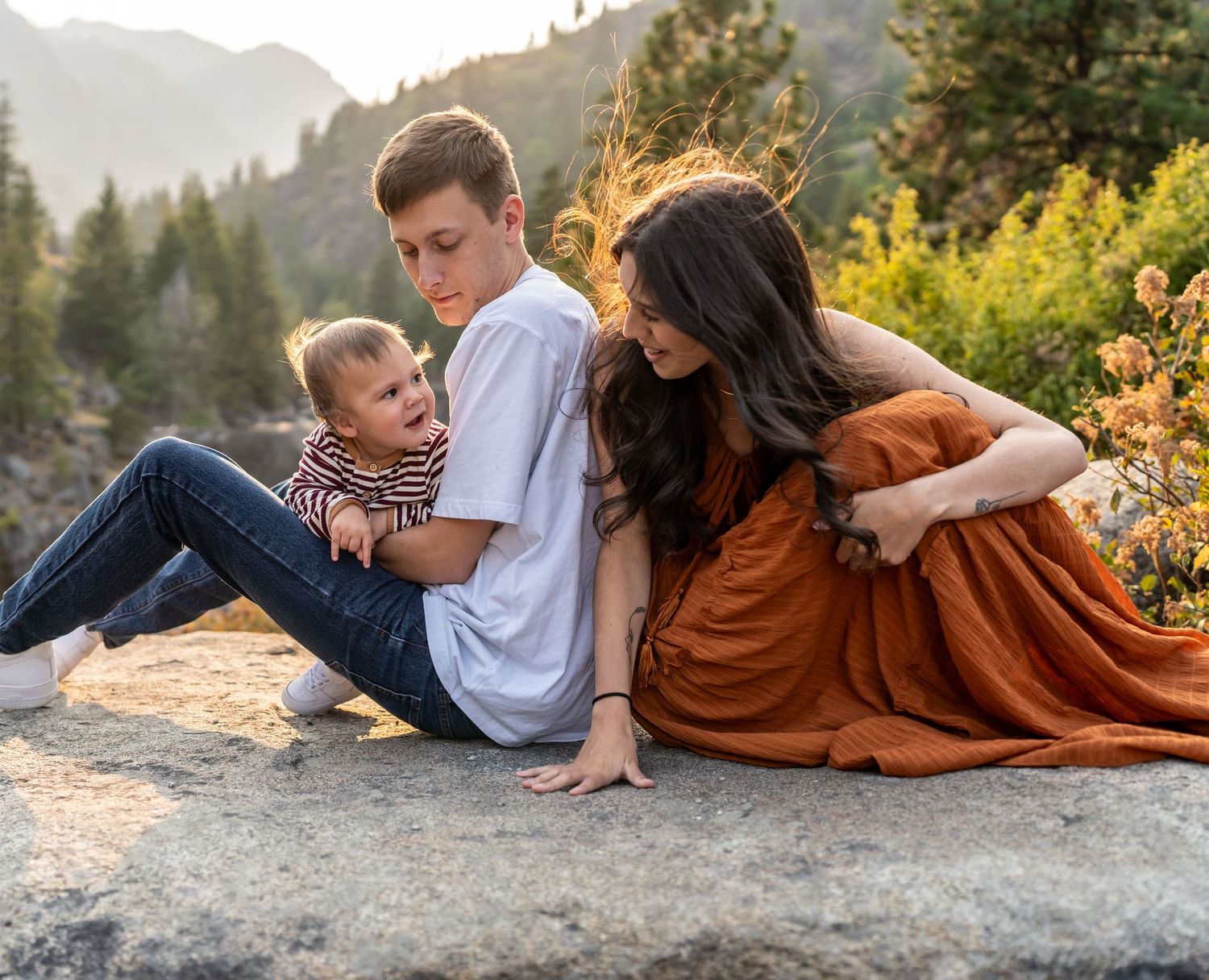 Family relaxing together on a rocky mountain ledge during sunset.