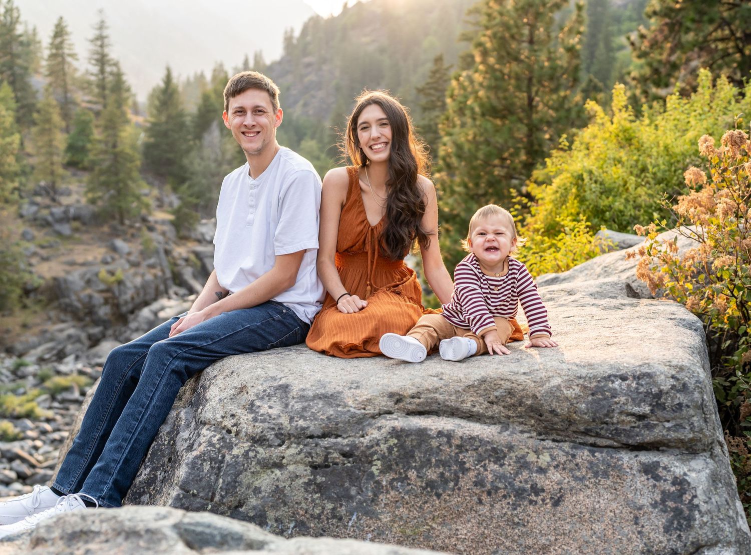 Family sitting together on a large boulder with mountain scenery in the background.