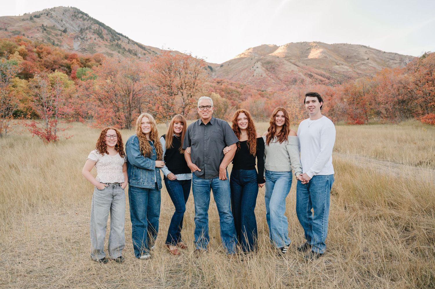 Family portrait session in golden field with mountains and autumn colors in the distance.