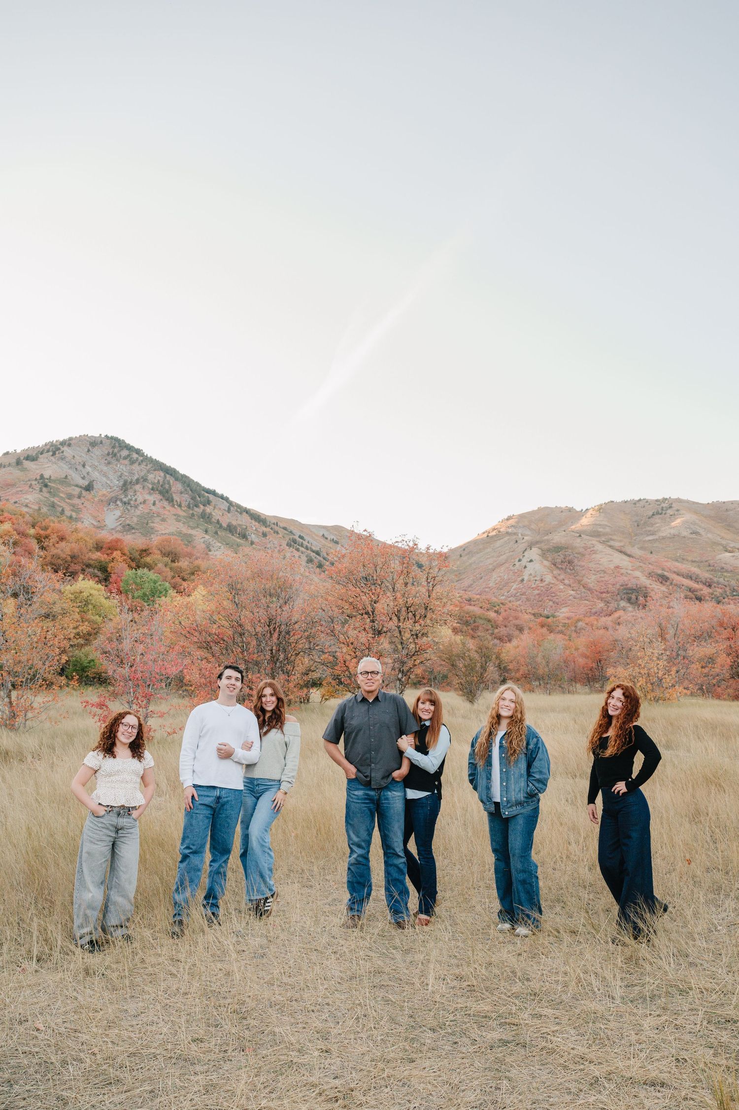 A group stands together in a field with autumn mountains and foliage creating a scenic backdrop.