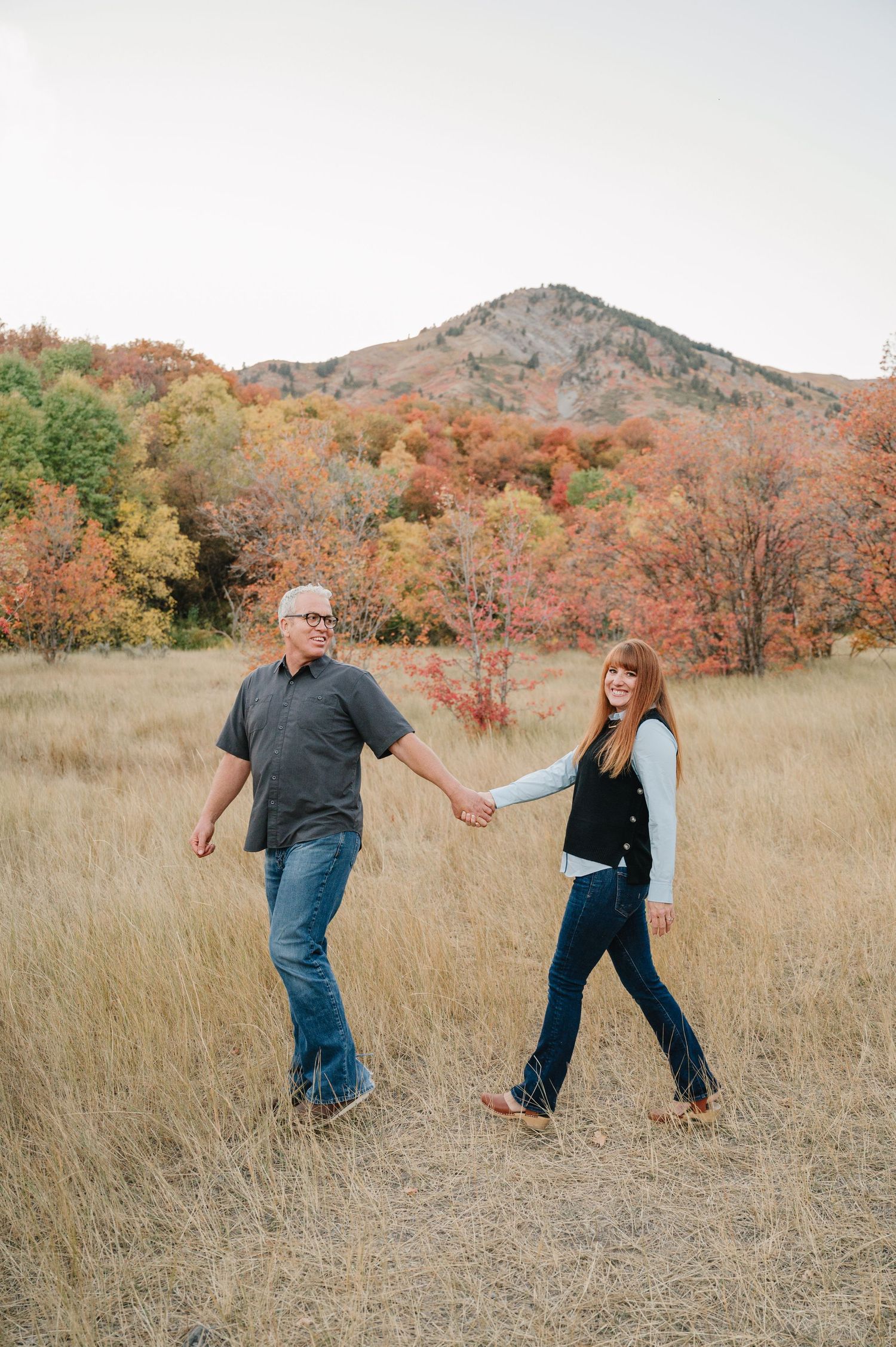A couple dances playfully together in a golden autumn field with mountains and fall foliage in the background.
