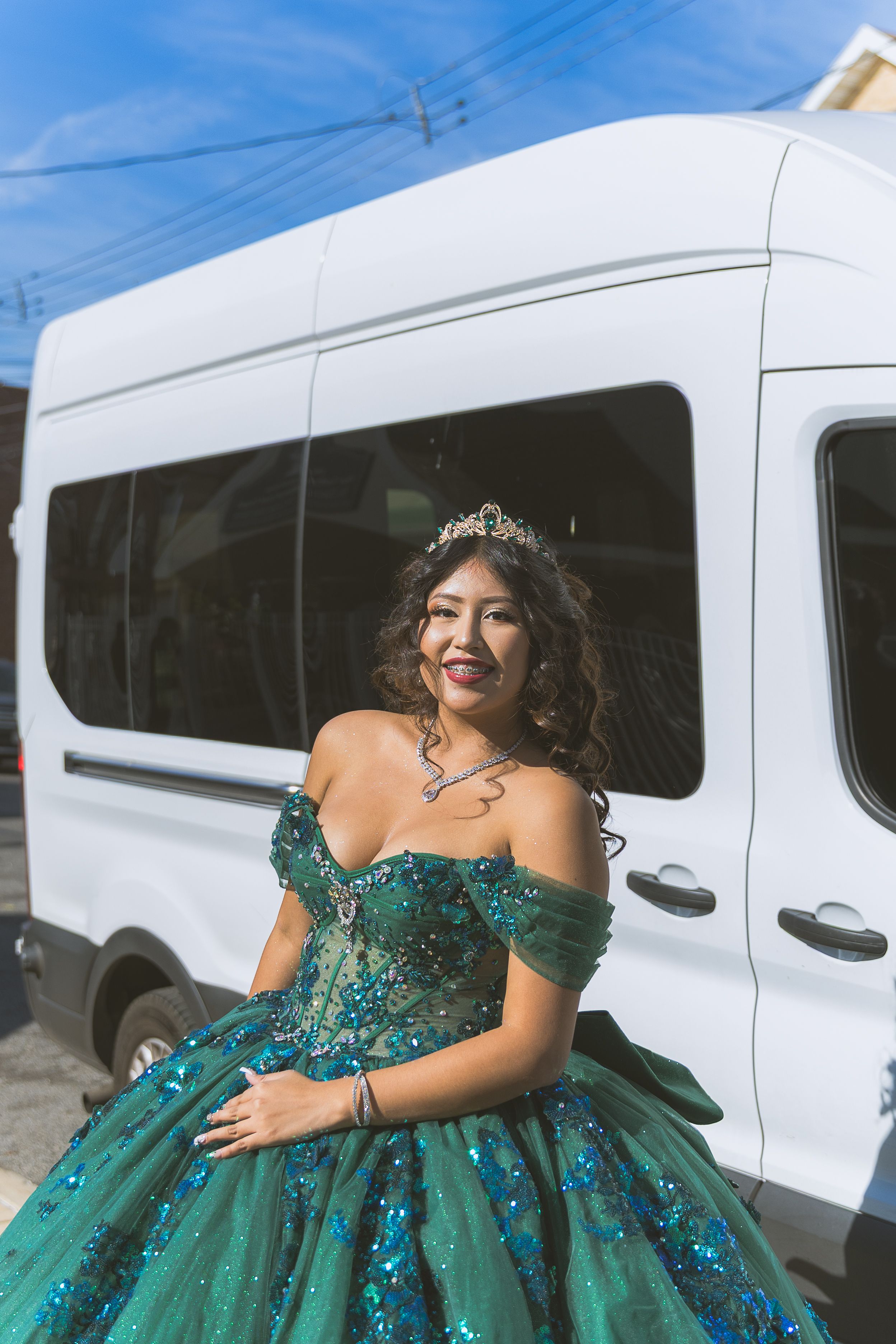 A person in an emerald green ball gown poses elegantly next to a white van outdoors.
