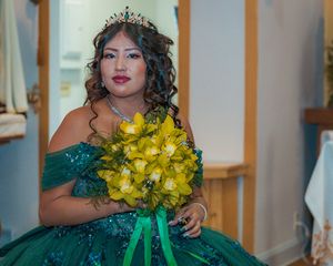 Elegant green ball gown with yellow bouquet and tiara in formal portrait.