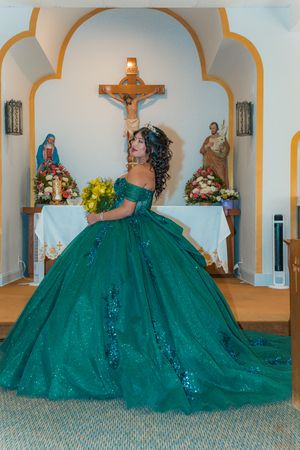 Dramatic emerald green ball gown with full skirt photographed in church setting.