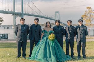 Wedding party poses in front of bridge wearing emerald dress and dark suits.