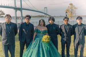 Formal group photo with emerald gown and suits against scenic bridge backdrop.