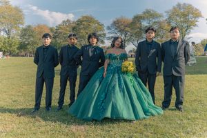 Wedding party stands on grass with bridge in background wearing coordinated green and black attire.