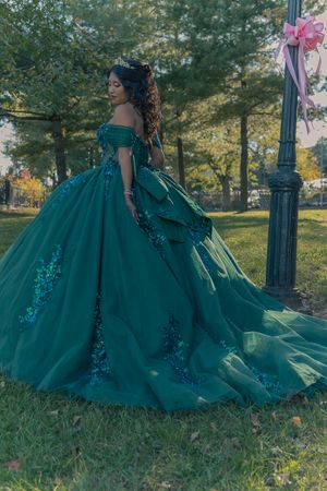 Elegant emerald ballgown with sequin details photographed in park setting.