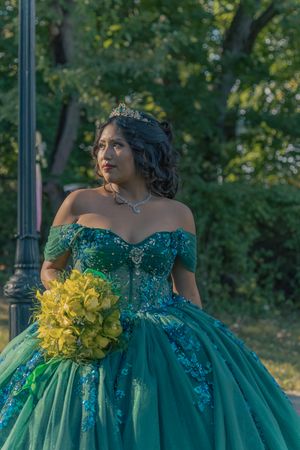 A stunning emerald green ball gown with beaded details and yellow floral bouquet in an outdoor garden setting.