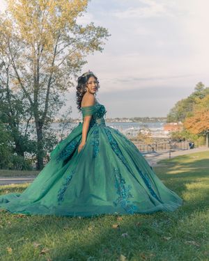 Emerald green quinceañera dress with full skirt photographed on grassy hill with waterfront view.