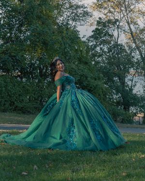 Dramatic emerald ballgown with full tulle skirt photographed against a natural outdoor landscape.