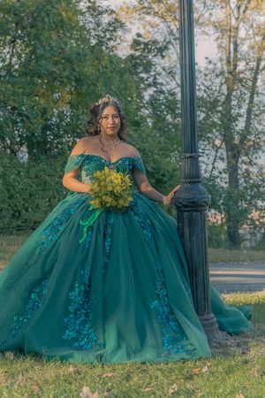 Elegant off-shoulder green gown with sequin details and yellow bouquet captured in a park setting.