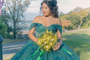 Elegant portrait in emerald green ball gown holding yellow orchids against natural backdrop.