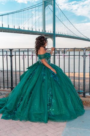 Stunning emerald quinceanera dress photographed near waterfront with bridge in background.