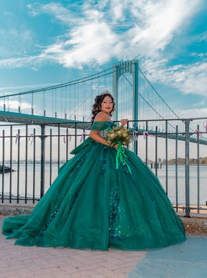 Emerald green ballgown photographed against bridge backdrop with dramatic flowing skirt and off-shoulder design.