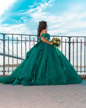 Elegant green ball gown with sequins captured in outdoor photoshoot by metal railing.