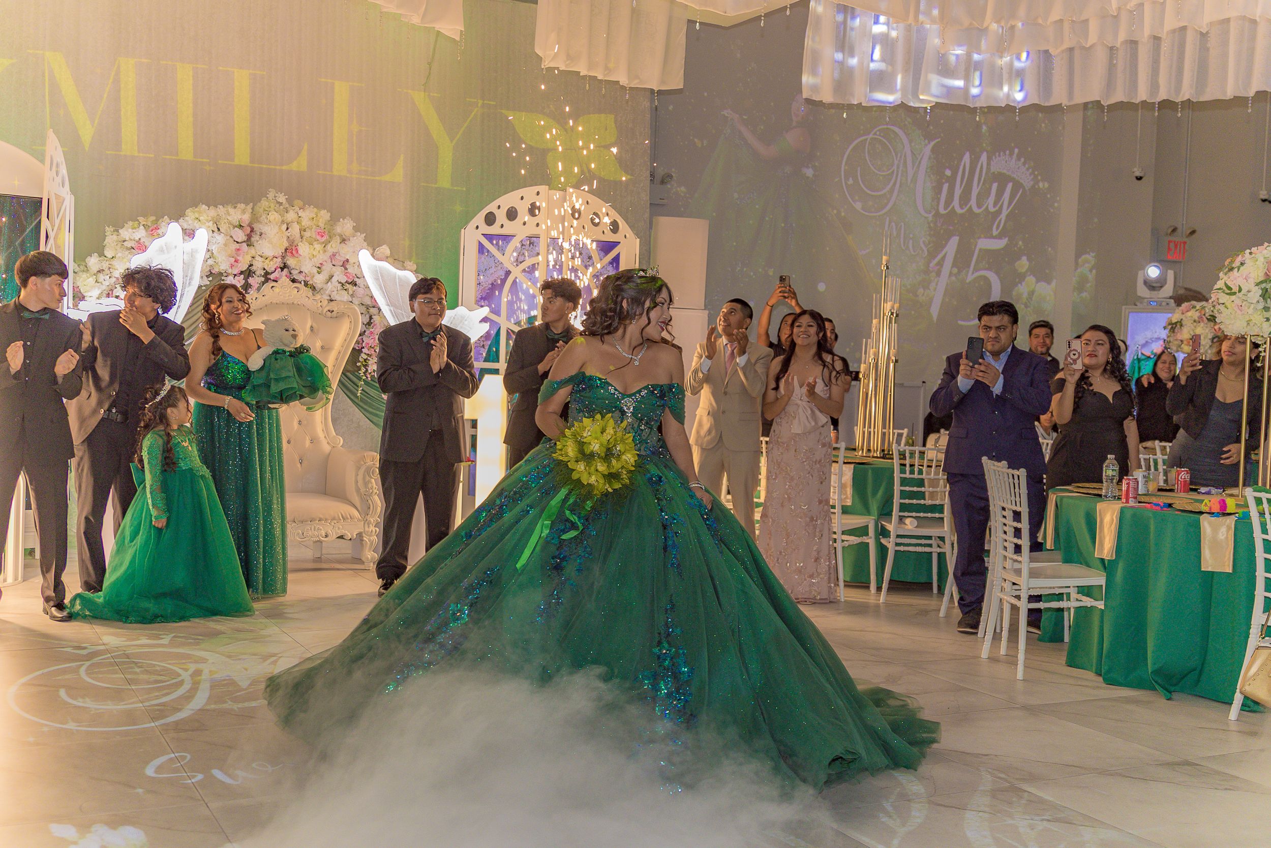 A grand ballroom decorated in green with guests seated at round tables for a formal event.