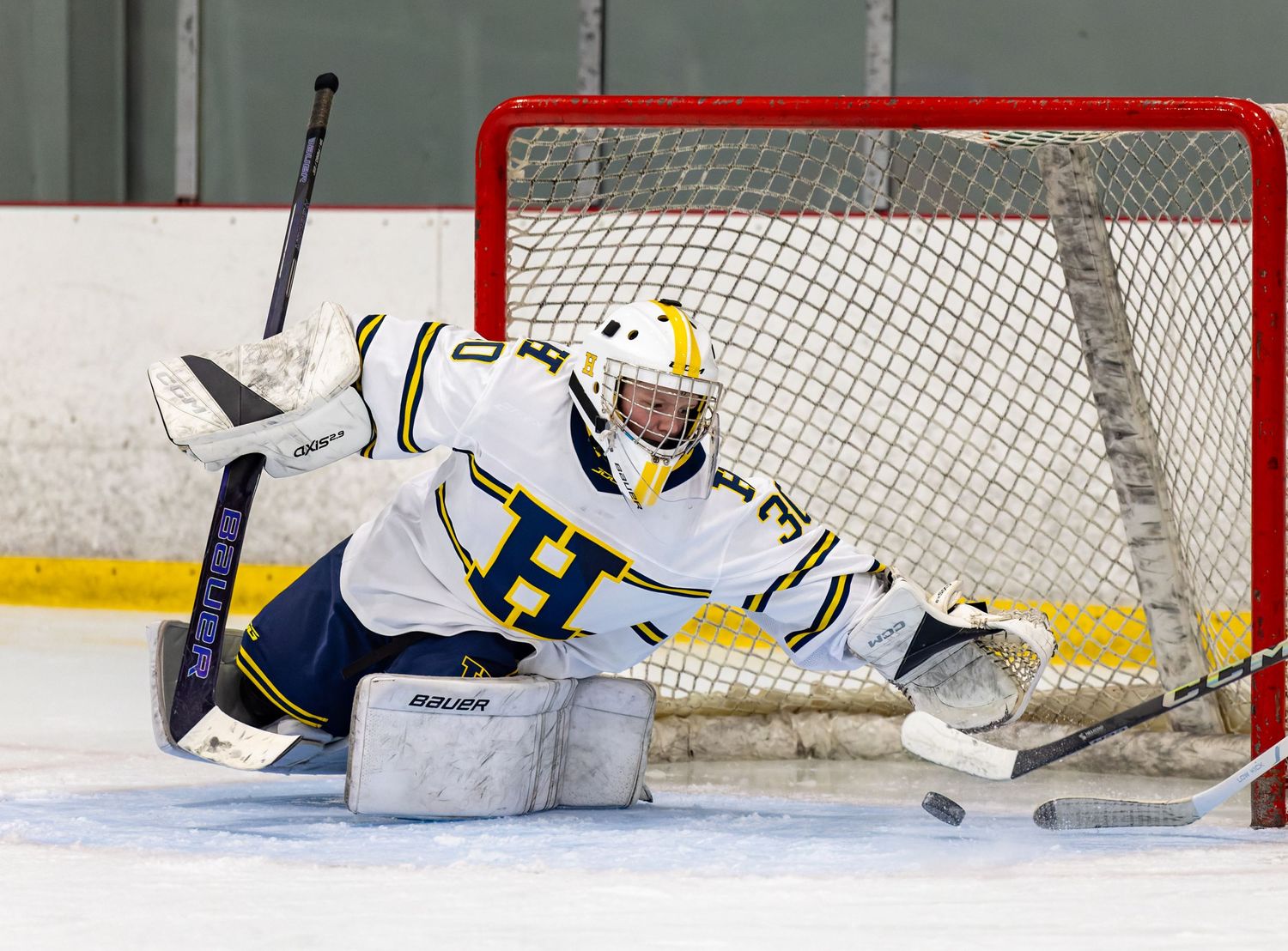 A hockey goalie makes a dramatic save by stretching out across the ice to block the puck.