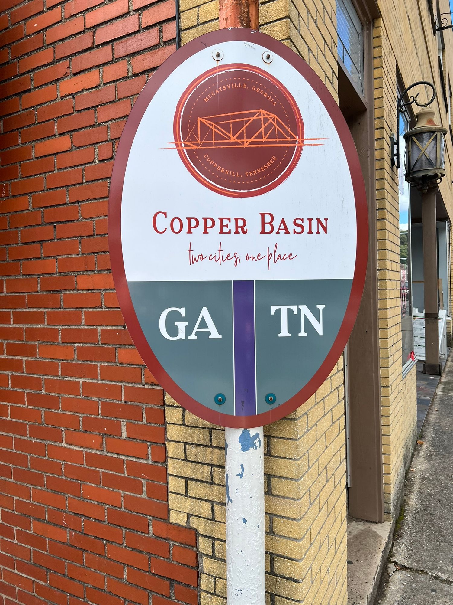 An oval Copper Basin sign marking the Georgia and Tennessee border mounted on a brick building wall.