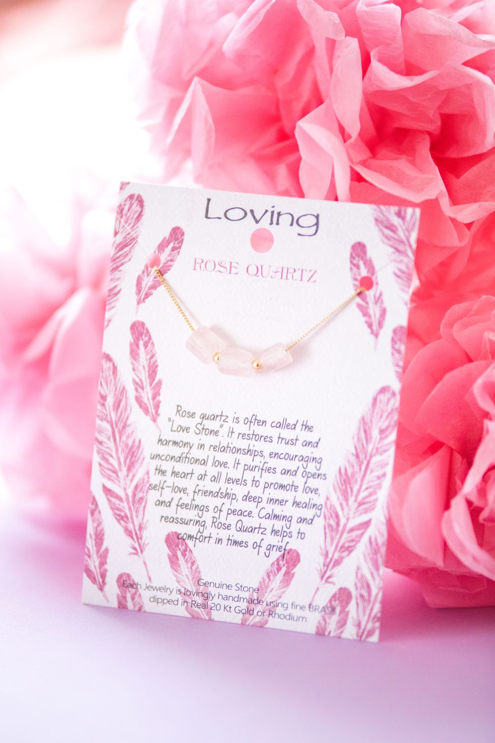 Pink feather-decorated 'Loving' jewelry card with necklace against rose background.