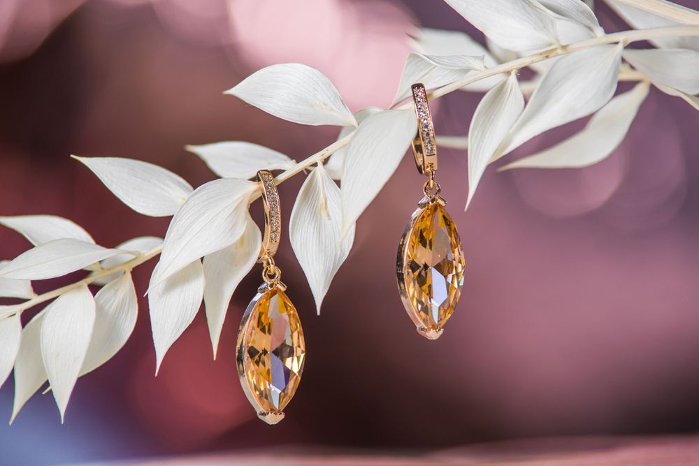 Elegant golden drop earrings with amber crystals hanging against white leaves.