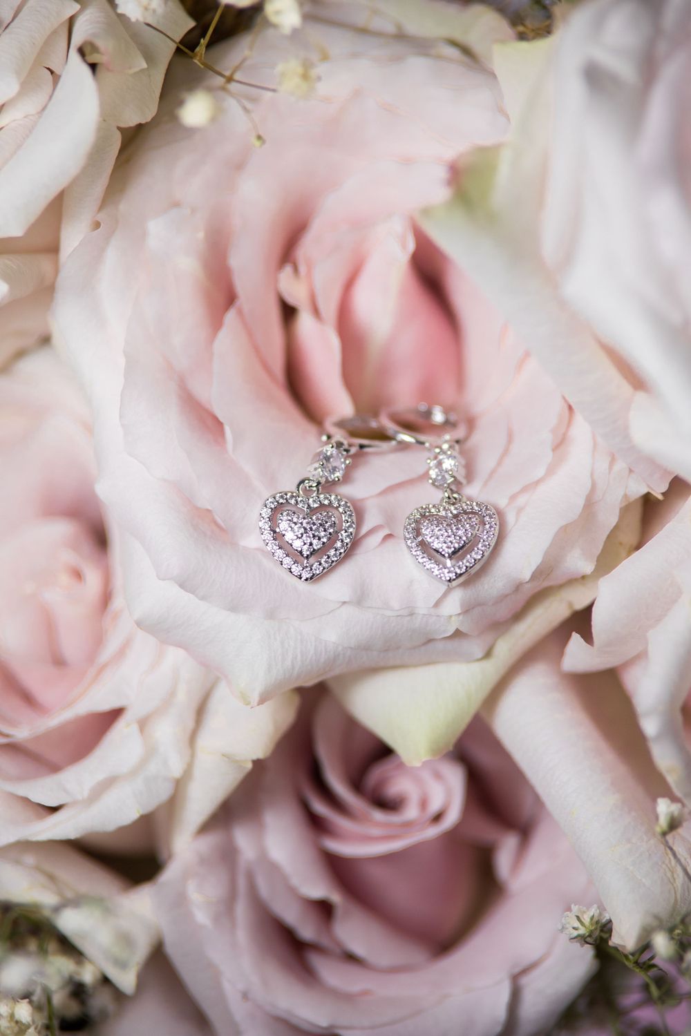 Heart-shaped diamond earrings nestled in soft pink rose petals.