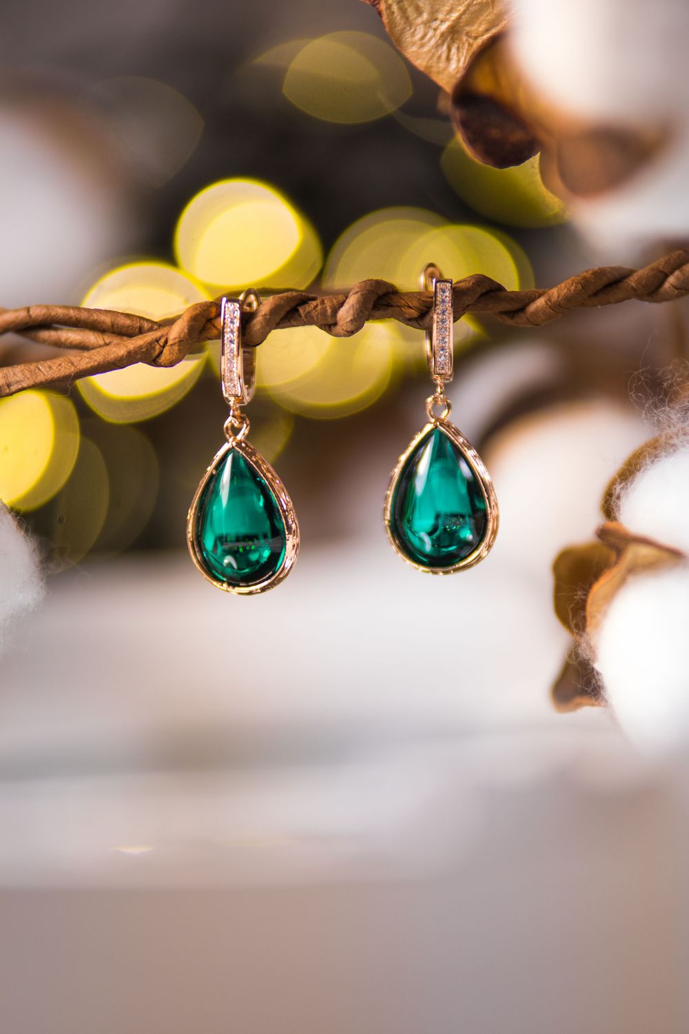 Emerald teardrop earrings with crystal accents captured against bokeh background.