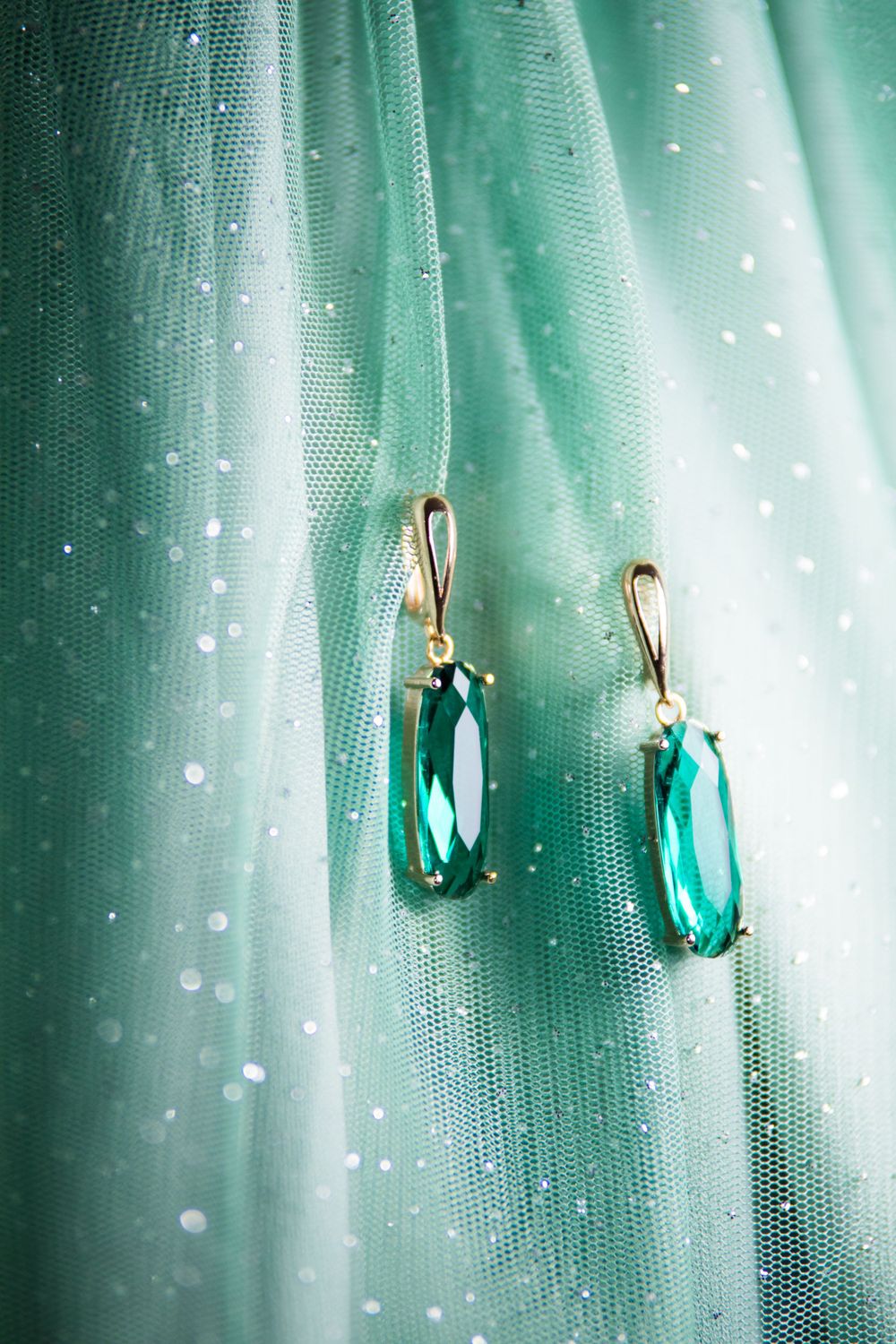 Elegant turquoise crystal drop earrings hanging against shimmery mint green fabric.