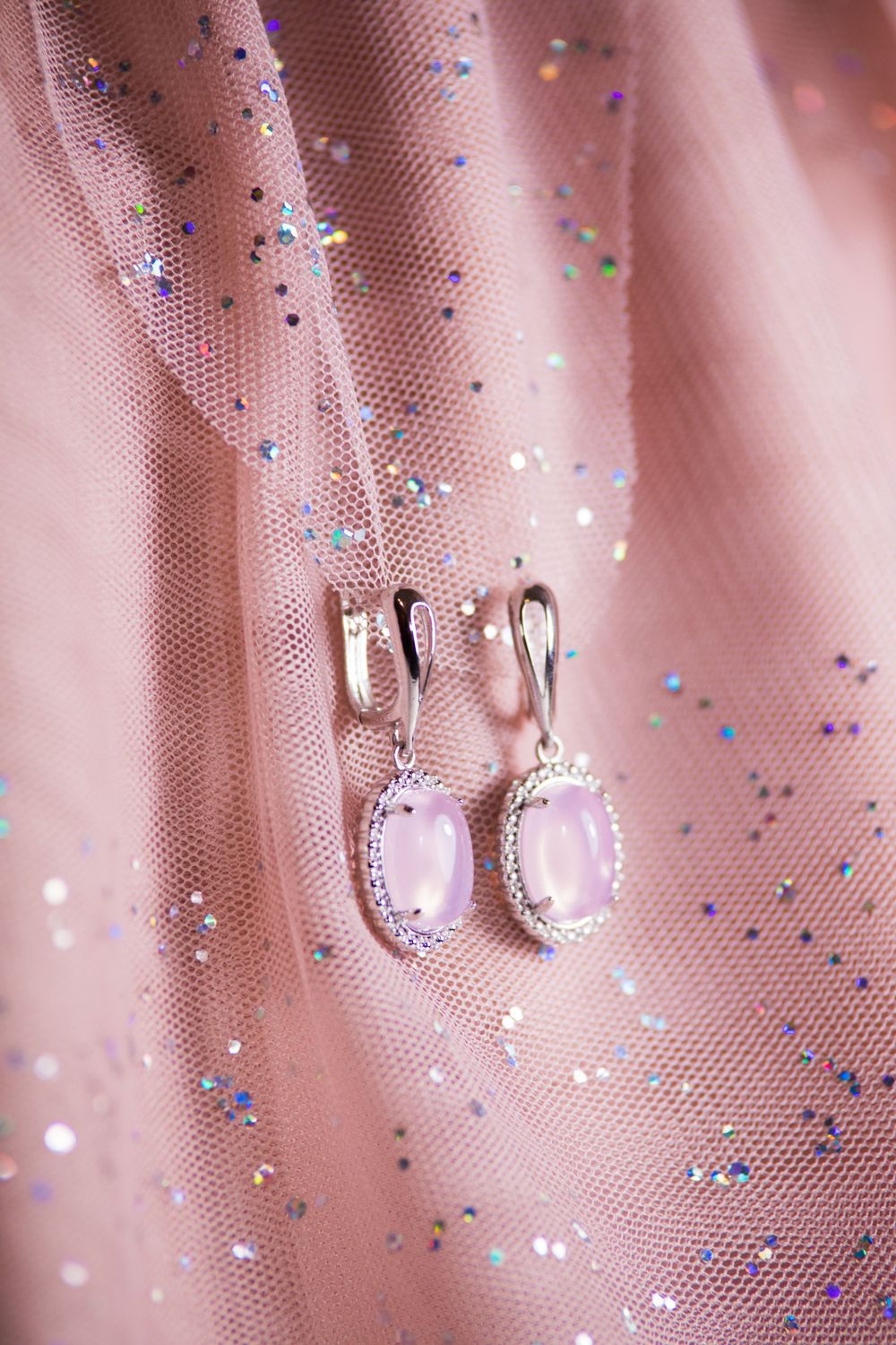 Pink gemstone earrings suspended against sparkly pink tulle fabric.