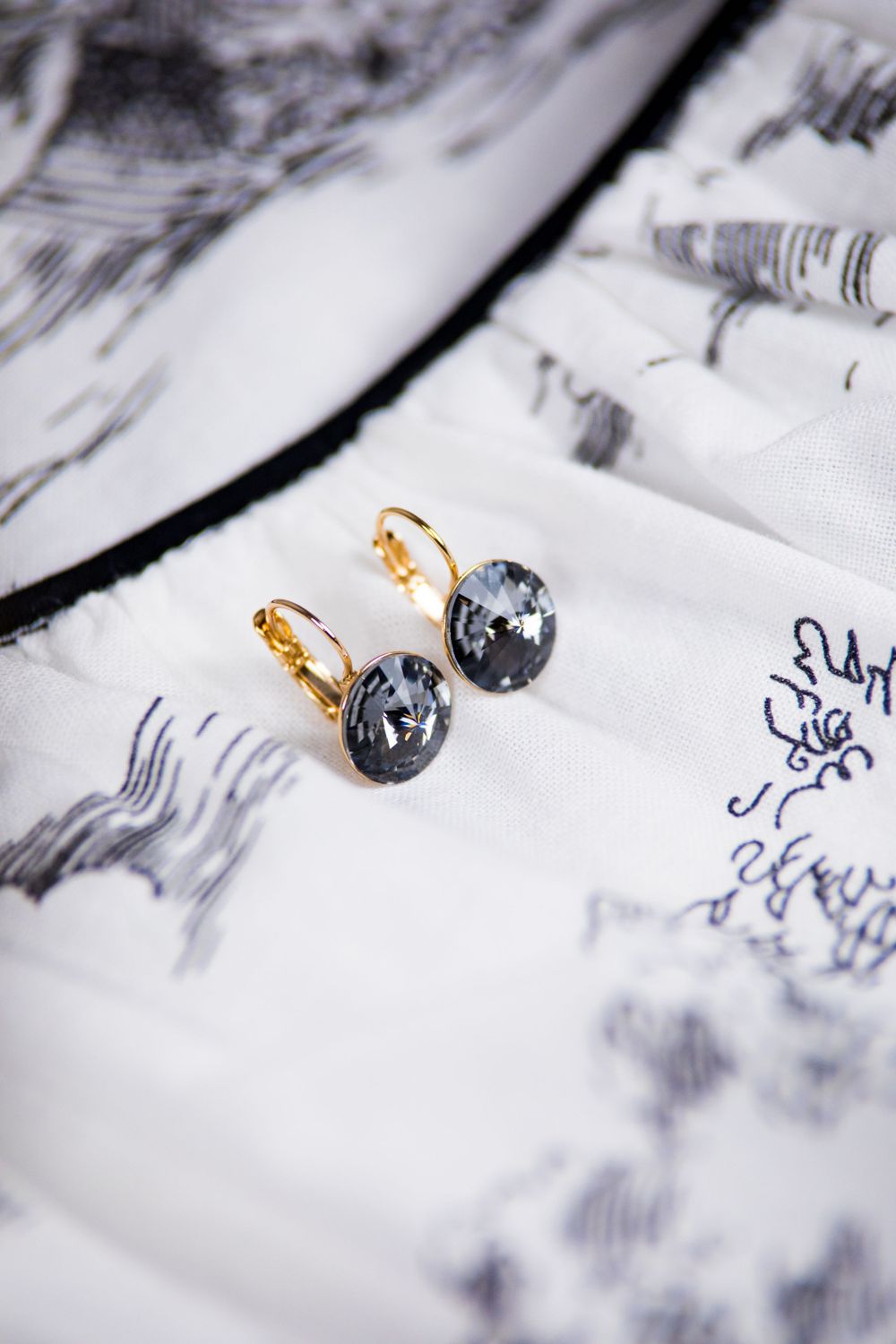 Gray stone drop earrings with gold clasps on marble-patterned surface.