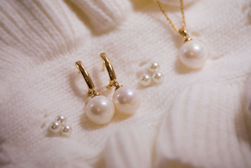 Pearl drop earrings and studs arranged on white knit fabric.