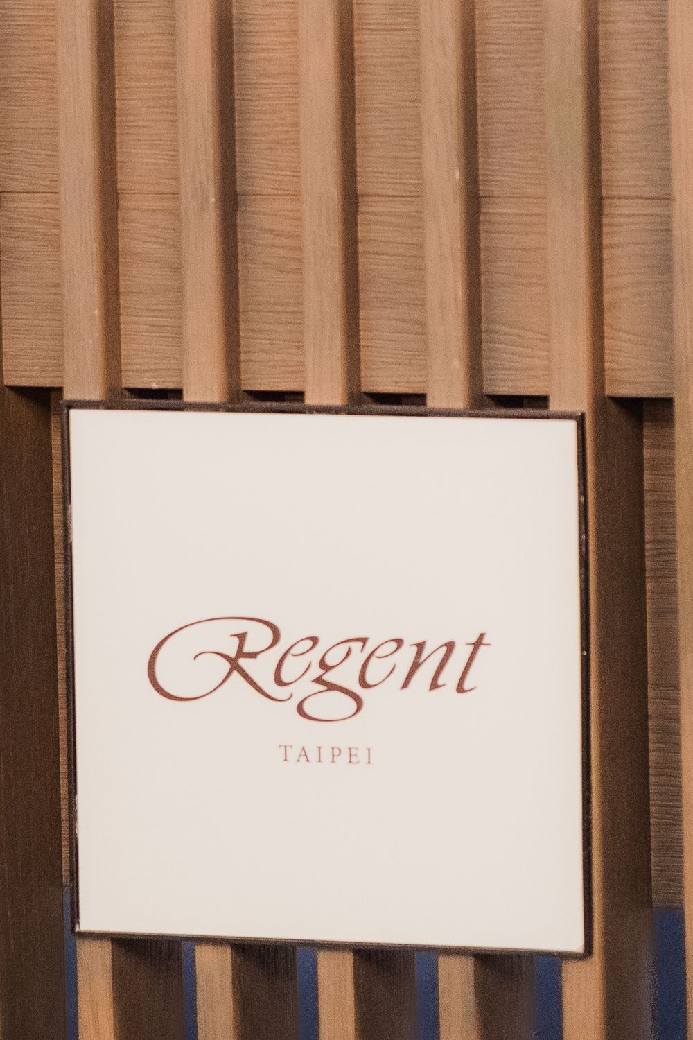 Modern interior wall design with wooden slats and illuminated Regent Taipei hotel signage mounted on the wall.