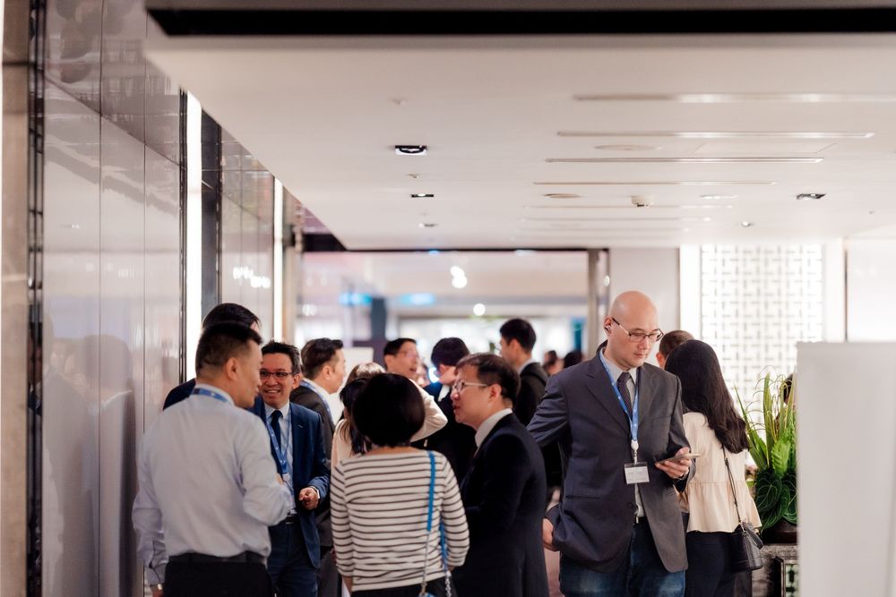 Business professionals gather in a modern office hallway for networking and conversation during a corporate event.