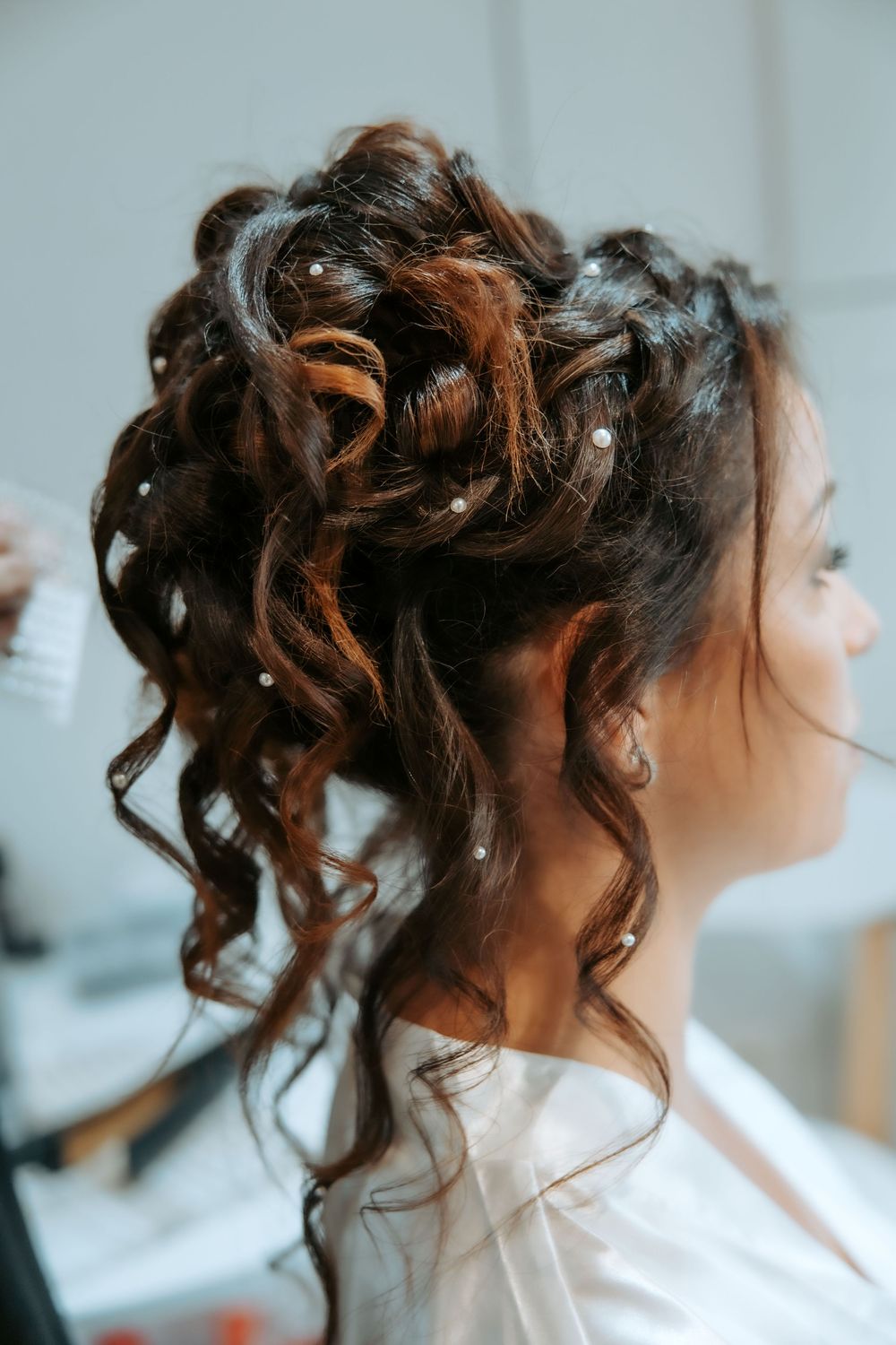 Close-up view of an elegant updo hairstyle with curled tendrils and pearl hair accessories against a light background.