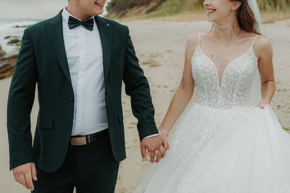 A wedding couple and their wedding party walking together on a sandy beach in formal attire.