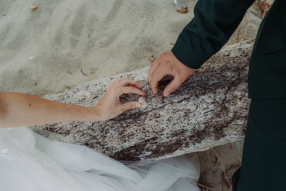 Close-up detail shot of a white wedding dress fabric against dark rocks at the shoreline.