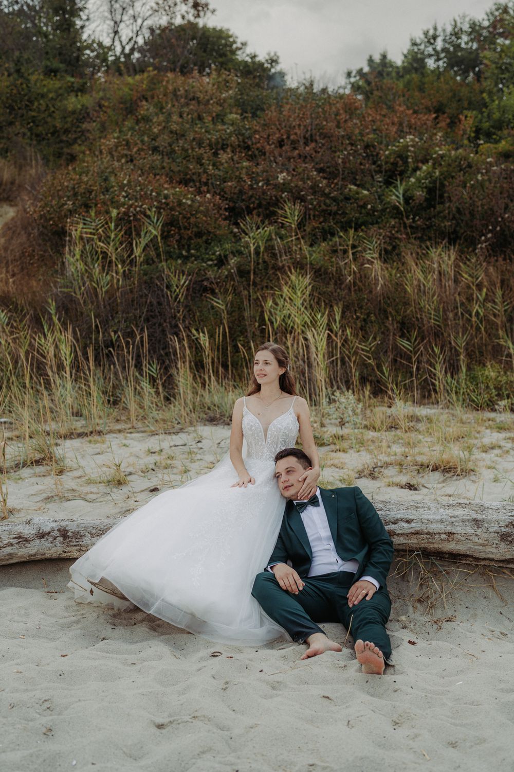 A romantic wedding photoshoot sequence shows a couple sitting together on a sandy beach near coastal vegetation.