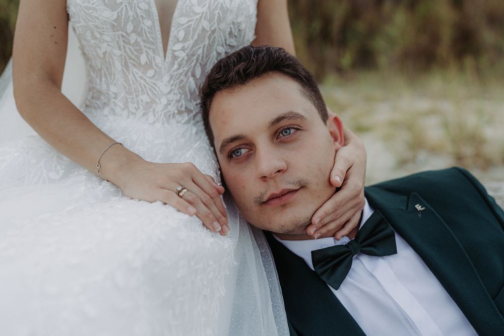 Close-up portrait of newlyweds with bride in white lace dress and groom in dark tuxedo with bowtie.