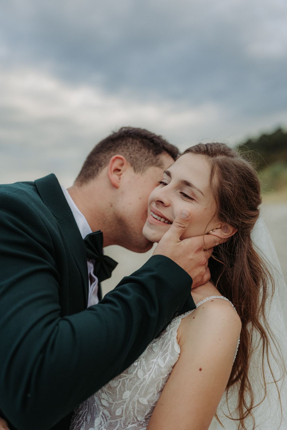 Intimate seaside wedding moment captured with cloudy coastal backdrop.