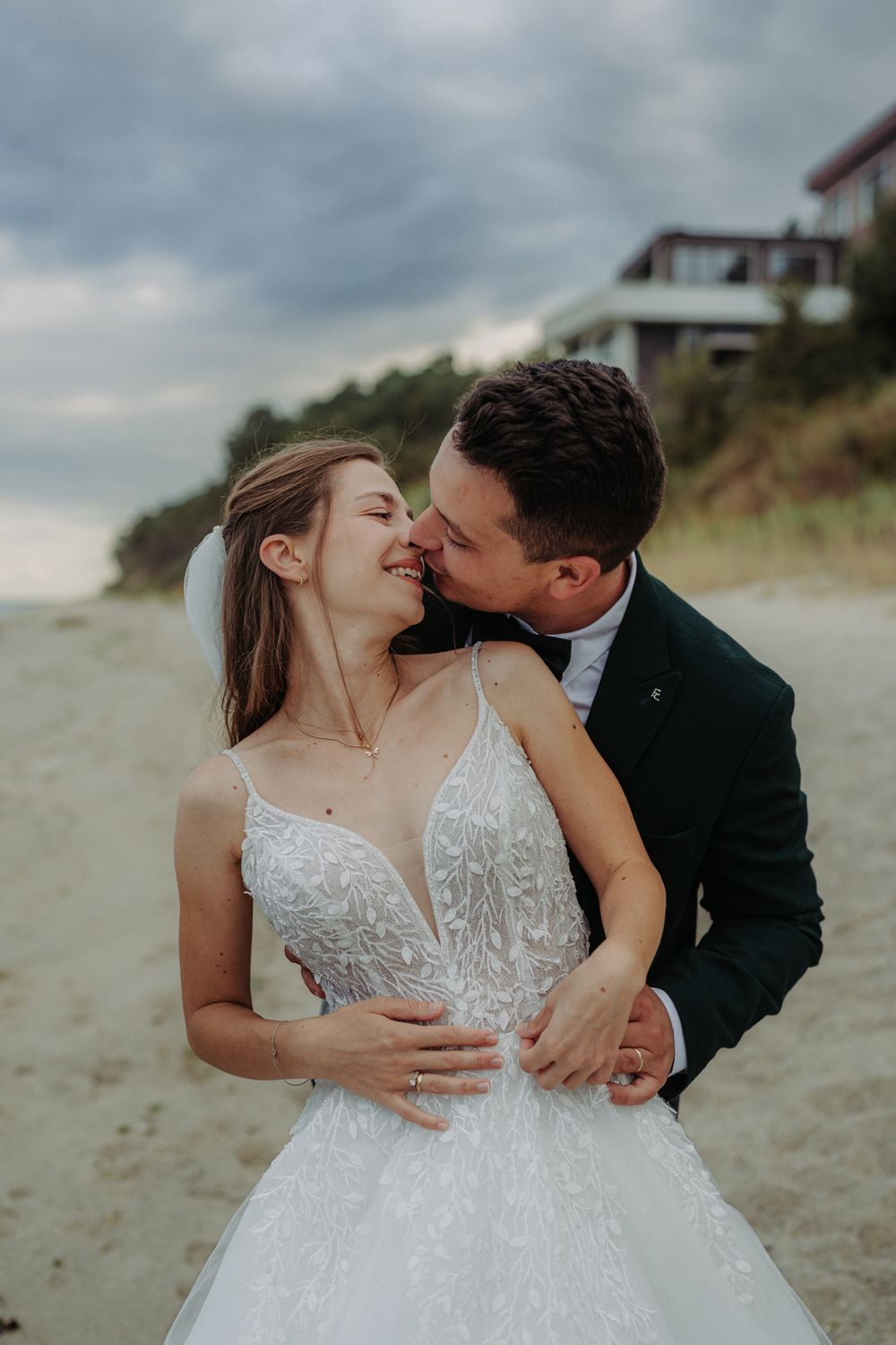 Romantic beach wedding photo series showing newlyweds sharing intimate kisses against a moody coastal backdrop.