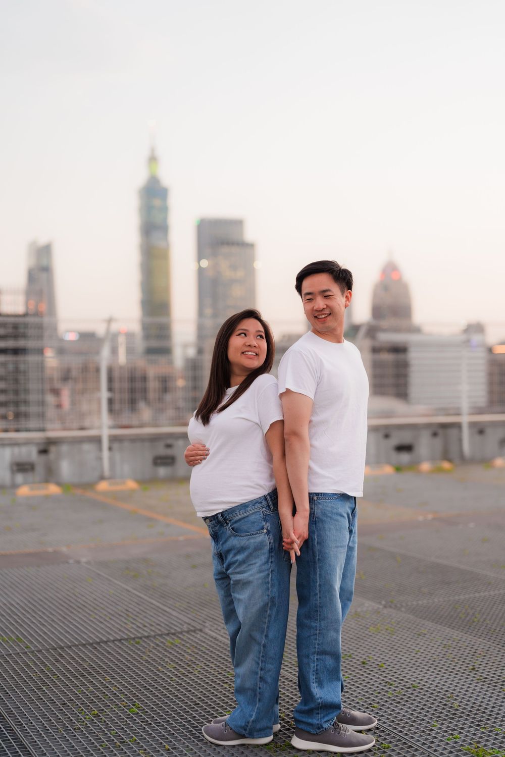 A couple shares a romantic moment on a rooftop overlooking a city skyline at dusk.