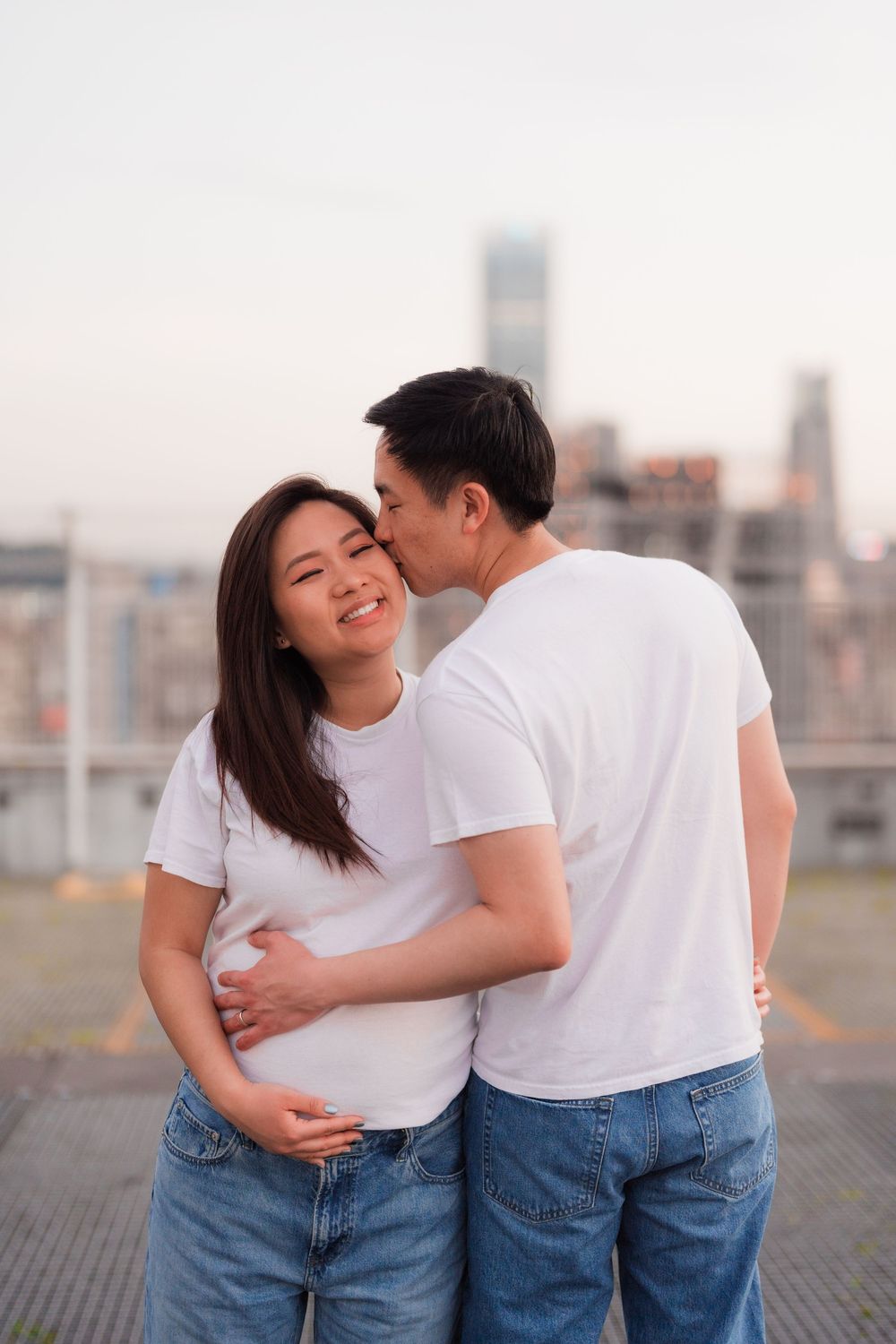 A couple in matching white t-shirts and jeans share tender moments against a city skyline backdrop.