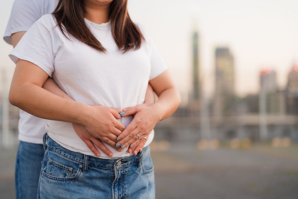 Person wearing a white t-shirt and blue jeans poses casually against an urban backdrop at sunset.