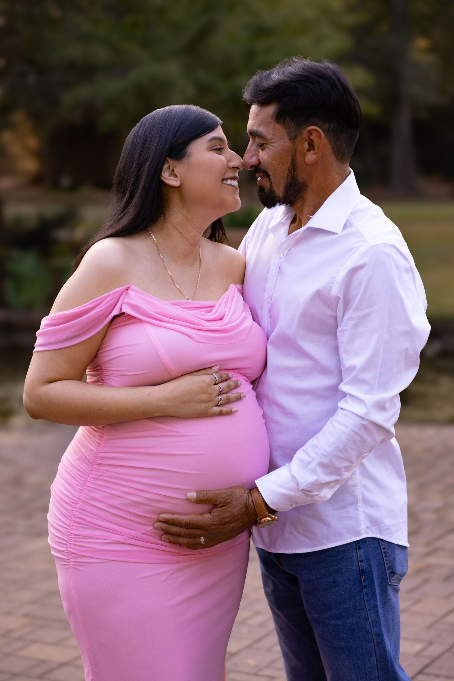 Intimate maternity portrait of couple in pink dress and white shirt on brick pathway during golden hour at Mercer Botanic Garden in Houston