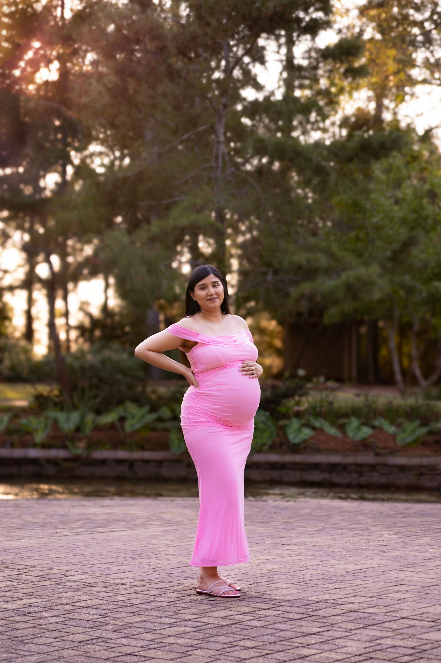 Pregnant woman in pink dress poses during sunset maternity photoshoot at Mercer Botanic Garden in Houston Tx.