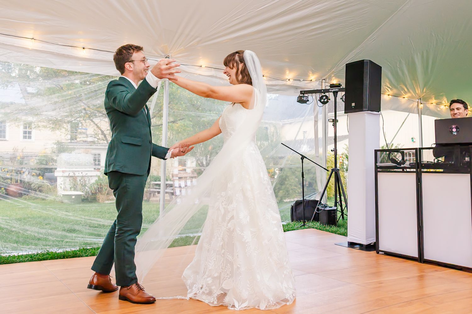 A couple dances together during their first dance at a wedding reception under white tent lighting.