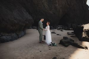 A couple in wedding attire shares an intimate moment on a rocky beach during their coastal ceremony.