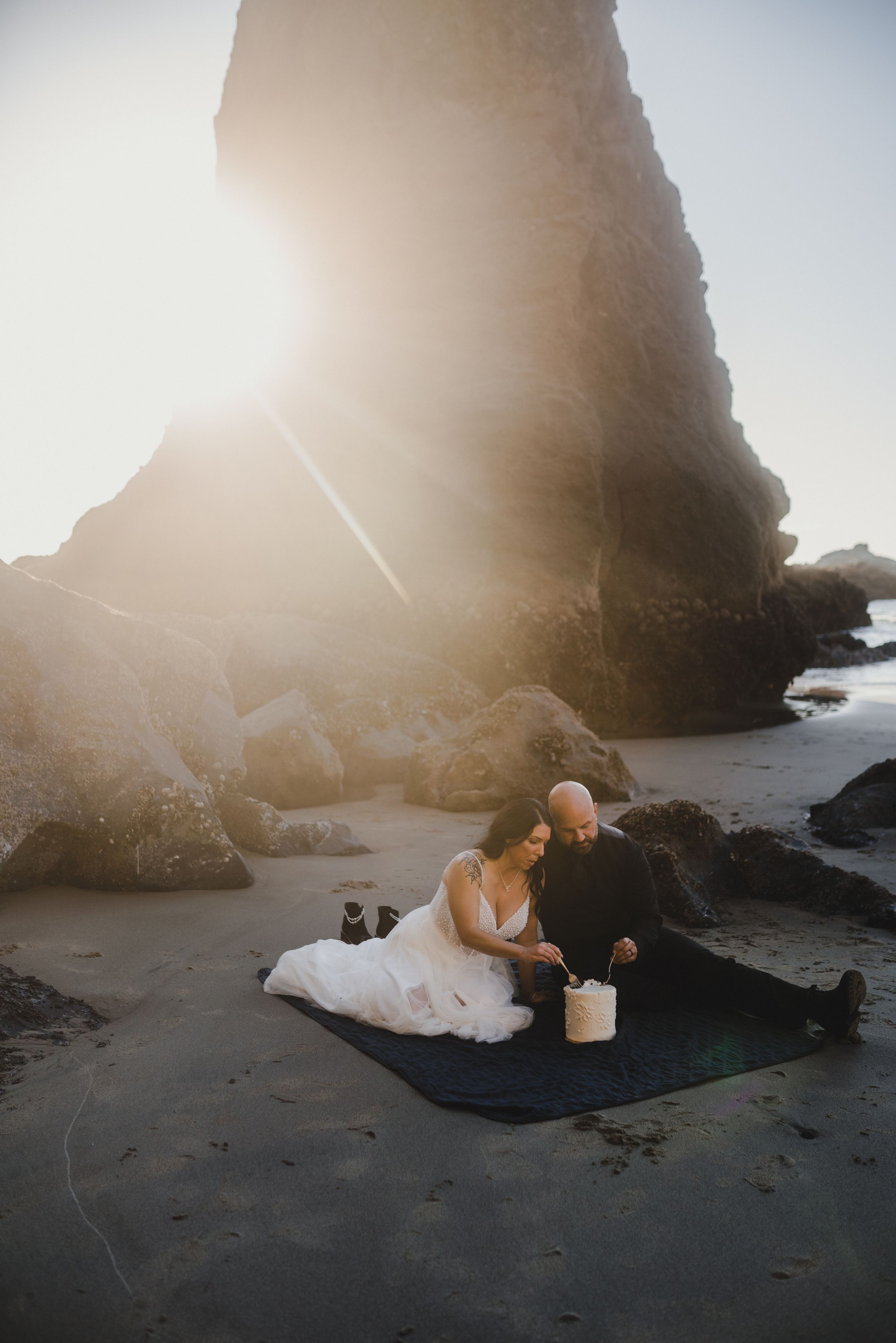 Romantic couple embracing on a misty beach at sunset with dramatic rock formations in the background.